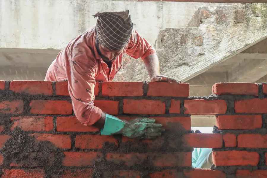 Mason laying a course of red brick with a trowel