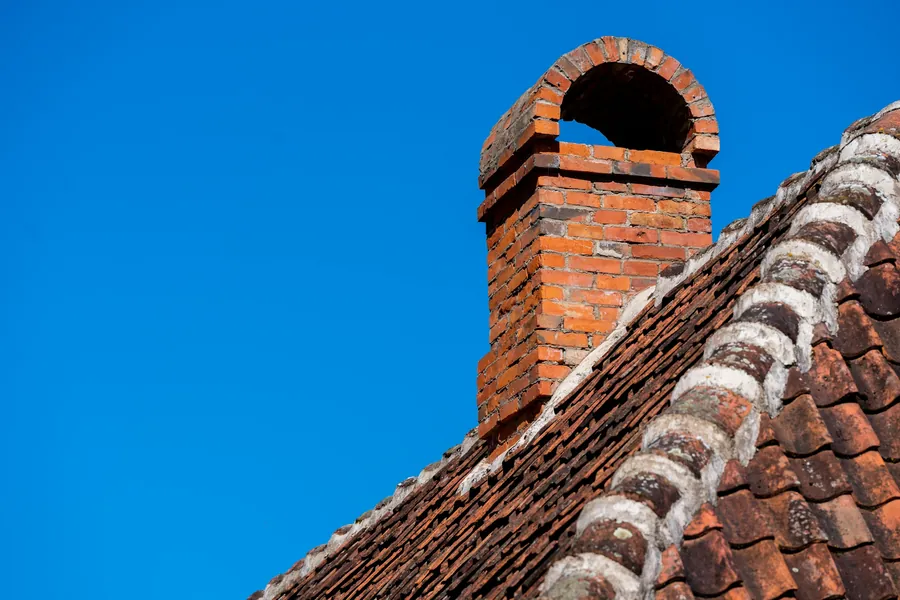 Red brick chimney rebuilt above a roof line against a clear sky